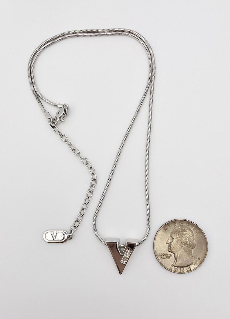 May include: A silver chain necklace with a silver pendant shaped like the letter V. The pendant has two small clear stones. The necklace is about 18 inches long.