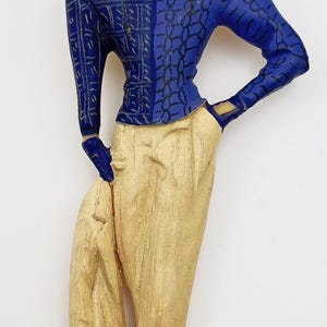 May include: A blue and white patterned figurine of a woman wearing a blue hat, a blue and white patterned shirt, and beige pants.