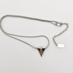 May include: A silver chain necklace with a silver V-shaped pendant. The chain is a snake chain style.