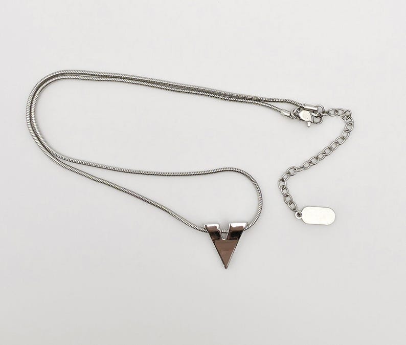 May include: A silver chain necklace with a silver V-shaped pendant. The chain is a snake chain style.