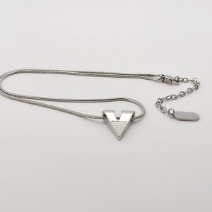 May include: A silver necklace with a V-shaped pendant. The necklace has a snake chain and a lobster clasp.