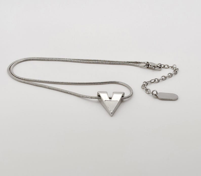 May include: A silver necklace with a V-shaped pendant. The necklace has a snake chain and a lobster clasp.
