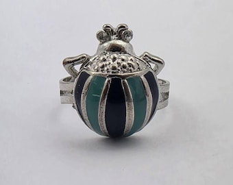 May include: A silver ring with a green and black striped beetle design.