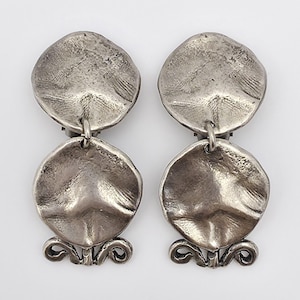 May include: A pair of silver tone dangle earrings with two round discs on each earring. The discs have a textured, hammered look.