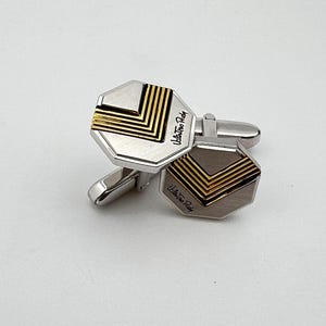 Puede incluir: Un par de gemelos de plata con un diseño geométrico en oro. Los gemelos están grabados con el texto "Ultra Fine Ruby".