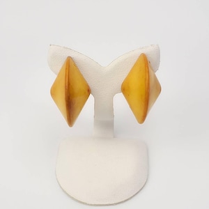 May include: A pair of yellow, diamond-shaped earrings on a white display stand.