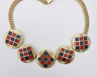 Puede incluir: Un collar dorado con una cadena y cinco colgantes circulares. Cada colgante presenta un diseño a cuadros rojo y azul marino. Este collar es una pieza llamativa, perfecta para añadir un toque vintage a cualquier atuendo.