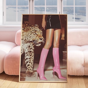 May include: A framed art print featuring a leopard and a person wearing a black skirt and pink high-heeled boots. The artwork is displayed in a pink room with a matching sofa and a view of a cityscape through a large window.