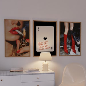 May include: Three framed prints on a white wall. The left print features a woman with red lips and a lit cigarette. The middle print is a black and white playing card with the text "Make Love Make Art Make Out Make Money". The right print shows a pair of legs wearing red boots and a black panther.