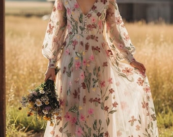 May include: A long, flowing wedding dress with a V-neck and long sleeves. The dress is adorned with embroidered pink, yellow, and burgundy flowers and green leaves. A floral crown and a bouquet of flowers complete the look.