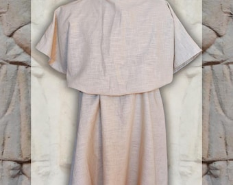 May include: A beige, short-sleeved tunic featuring a loose, draped upper layer that falls over the shoulders and chest, transitioning into a simple, straight-cut skirt that reaches above the knees, crafted from a textured, woven fabric.
