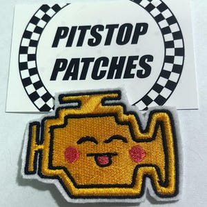 May include: Yellow embroidered patch of a car engine check light with a smiling face and pink cheeks. The patch has black outlines and is on a white background. The text "PITSTOP PATCHES" is on a white background with a black and white checkered circle.