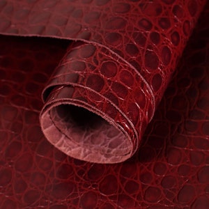 May include: A roll of burgundy faux crocodile embossed leather. The leather has a textured, pebbled surface.