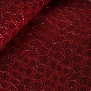 May include: Close-up of a red faux leather fabric with a crocodile skin pattern.