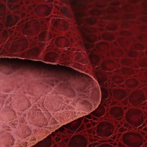 May include: Close-up of a burgundy leather fabric with a textured alligator pattern.