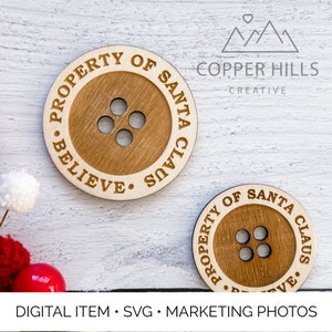 May include: Two wooden round ornaments with a button design. The ornaments are engraved with the text "Property of Santa Claus. Believe." and "Property of Santa Claus. Believe."