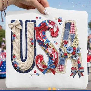 May include: White square with the word "USA" in red, white, and blue decorative letters. The "U" is a cream-colored knit design, the "S" is red sequins, and the "A" is patchwork. The image is held up in front of a parade.