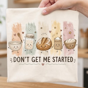 May include: A cream-colored fabric item featuring a colorful graphic of five cartoon baking items including a bowl, a jar, a loaf of bread, a flour bag, and a basket. The text DON'T GET ME STARTED is printed in black below the illustrations.