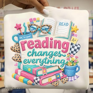 Könnte beinhalten: Ein weißes Sweatshirt mit einer bunten Grafik und dem Text reading changes everything. Das Design zeigt ein offenes Buch, eine Brille mit Leopardenmuster, eine blaue Tasse, gestapelte Bücher, einen Stift und florale Elemente in leuchtenden Farben.
