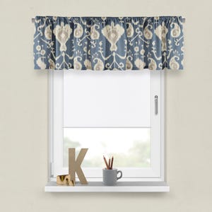 May include: A blue and white patterned valance with a ruffled edge. The valance is hung on a white window frame with a white window blind. A small gray cup with pencils and a wooden letter K are on the window sill.