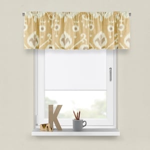 May include: A beige valance with a white ikat pattern hangs on a window. The valance is made of a soft, textured fabric. The window is white and has a white sill. There is a small wooden letter K and a cup with pencils on the sill.