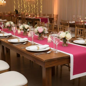 May include: A long wooden table set for a formal event, featuring a vibrant fuchsia runner with a white border. The table is adorned with white plates, silverware, and floral centerpieces, creating an elegant ambiance. Wine glasses and candles add to the sophisticated setting.