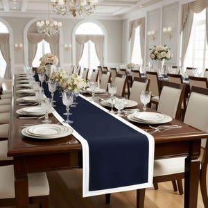 May include: A formal dining table set for a large gathering. The dark wood table is adorned with white plates, crystal glasses, and a navy blue table runner with a white border. Floral centerpieces and chairs complete the elegant setting.