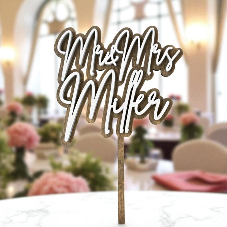 A wooden wedding cake topper with the names "Mrs & Mrs Miller" written on it.