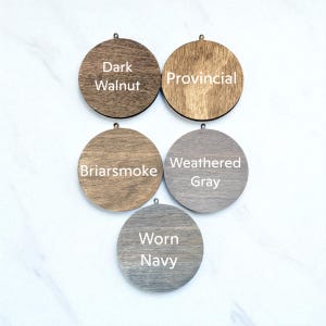 five wooden ornaments with different colors and finishes, including dark walnut, Provincial, Briarsmoke, Weathered Gray, and Worn Navy.