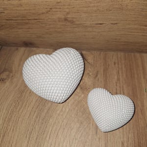 Könnte beinhalten: Zwei weiße herzförmige Dekorationsgegenstände mit strukturierter Oberfläche. Sie liegen auf einer Holzoberfläche. Das größere Herz ist diagonal positioniert, das kleinere rechts.