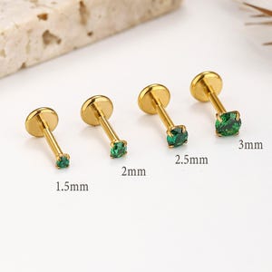 May include: Four gold-colored stud earrings with round, flat backs and slender posts. Each earring features a square, emerald-green gemstone. Sizes are 1.5mm, 2mm, 2.5mm, and 3mm. The earrings are displayed on a light background.
