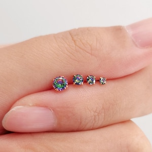 May include: Four round stud earrings featuring iridescent, multi-colored stones set in gold-toned metal prongs. The stones display a spectrum of green, blue, and purple hues, arranged in a row from the largest to the smallest size.