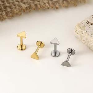 May include: Four small, triangle-shaped stud earrings in gold and silver tones. The earrings have a flat back and a post for piercing. The earrings are displayed on a white surface with a neutral background.
