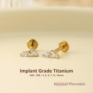 May include: Two gold-colored labret studs featuring a marquise-cut clear gemstone design. The text reads Implant Grade Titanium, 16G, 18G / 4, 5, 6, 7, 8, 10mm, and Internal Threaded. These earrings have a flat back post and a decorative front.