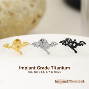 May include: Three stud earrings shaped like bats with pointed ears and tails, available in gold, silver, and black tones. The text reads Implant Grade Titanium, 16G, 18G / 4, 5, 6, 7, 8, 10mm, and Internal Threaded. These are flat-back body jewelry pieces.
