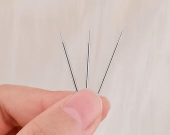 May include: Three slender, silver-toned metal acupuncture needles arranged in a fan shape. Each needle features a thin, straight shaft with a slightly thicker handle section at the base, designed for precision and professional use in therapeutic practice.