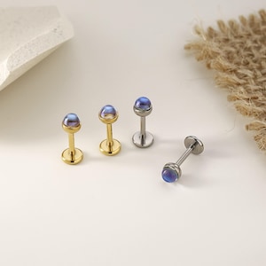 以下が含まれることがあります： 小さな虹色の青紫色のオーブが上部にある4つのジュエリー。3つはポストとベースがあり、2つは金色、1つは銀色です。4つ目のジュエリーは横に倒れています。