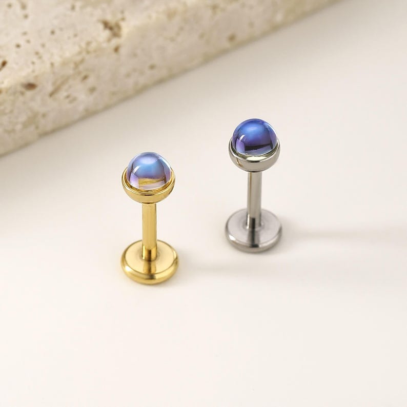 以下が含まれることがあります： イリデッセントブルーとゴールドトーンのトップが付いたスタッドピアス2つ。片方のイヤリングは金色、もう片方は銀色です。イヤリングは、さまざまなピアスに適したポストとフラットバックのデザインです。