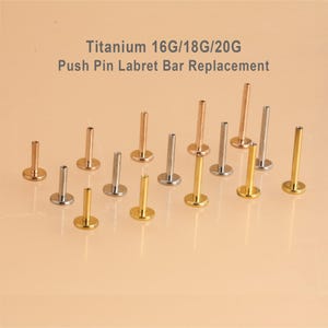 May include: An assortment of titanium labret bar replacements in gold, silver, and rose gold. The image includes the text "Titanium 16G/18G/20G Push Pin Labret Bar Replacement."
