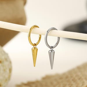 May include: Two hoop earrings, one gold-toned and one silver-toned, each featuring a smooth, conical spike charm suspended from the circular band. The earrings are displayed hanging side by side on a thin, light-colored horizontal rod.