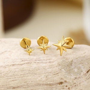 May include: Three gold-toned stud earrings, each featuring a multi-pointed star design. The earrings vary in size, with the smallest on the left and the largest on the right, all showcasing a polished metallic finish and a flat circular backing.