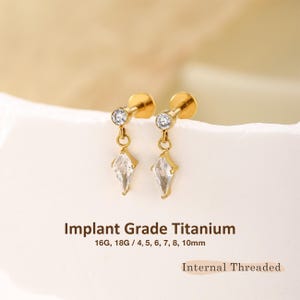 May include: Two gold-tone stud earrings featuring a round clear gemstone at the top and a dangling kite-shaped clear gemstone. The text reads Implant Grade Titanium, 16G, 18G / 4, 5, 6, 7, 8, 10mm, and Internal Threaded.