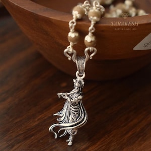 Puede incluir: Un collar con colgante de plata con una figura detallada tocando la flauta. El colgante cuelga de una cadena con cuentas decorativas. La imagen también muestra la marca "TARAKESH" y el texto "TRUSTED SINCE 1992".