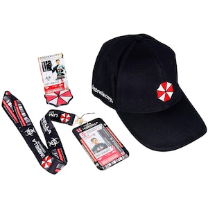 May include: A black baseball cap with a red and white umbrella logo, a lanyard, an ID badge, and a patch. The lanyard and ID badge feature the Umbrella Corporation logo and text. The cap has the text "Umbrellacorp." on the side.