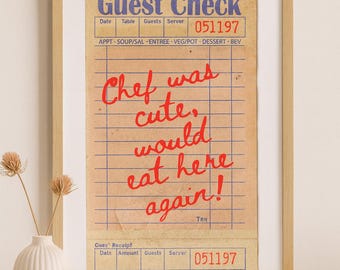 Könnte beinhalten: Gerahmter Druck eines Restaurantbelegs im Vintage-Stil. Der blaue Titel lautet "Guest Check", mit einer handschriftlichen roten Nachricht: "Chef was cute, would eat here again!" Ein dekoratives Element für Küche oder Esszimmer.