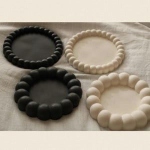 May include: Four round coasters with a raised, textured edge. Two coasters are black and two are white.