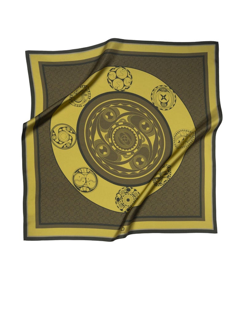 May include: A yellow silk scarf with a brown geometric design. The design features a large circle with smaller circles around it. The scarf is folded and draped over a white background.