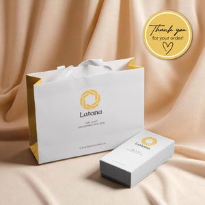 May include: A white gift bag and box with the Latona logo, a geometric design in yellow. The bag has a white ribbon handle and the text "silk scarf, your passion, love, story." A round sticker says "Thank you for your order!"