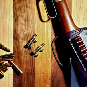 May include: A wooden surface with a rifle and a leather holster with bullets. There are also several brass casings on the surface.