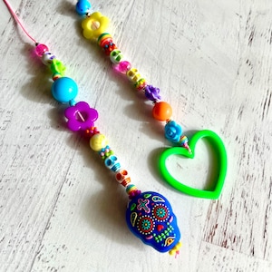 May include: Two beaded lanyards with colorful beads and charms. One lanyard features a blue skull charm with floral designs, while the other has a green heart-shaped charm. The beads include flowers, skulls, and various other shapes.